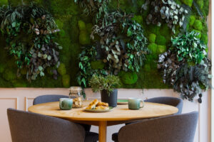 Table with 4 chairs in coffee area, in front of live green plant wall in BaseStack student accommodation and apartments to rent in Copenhagen