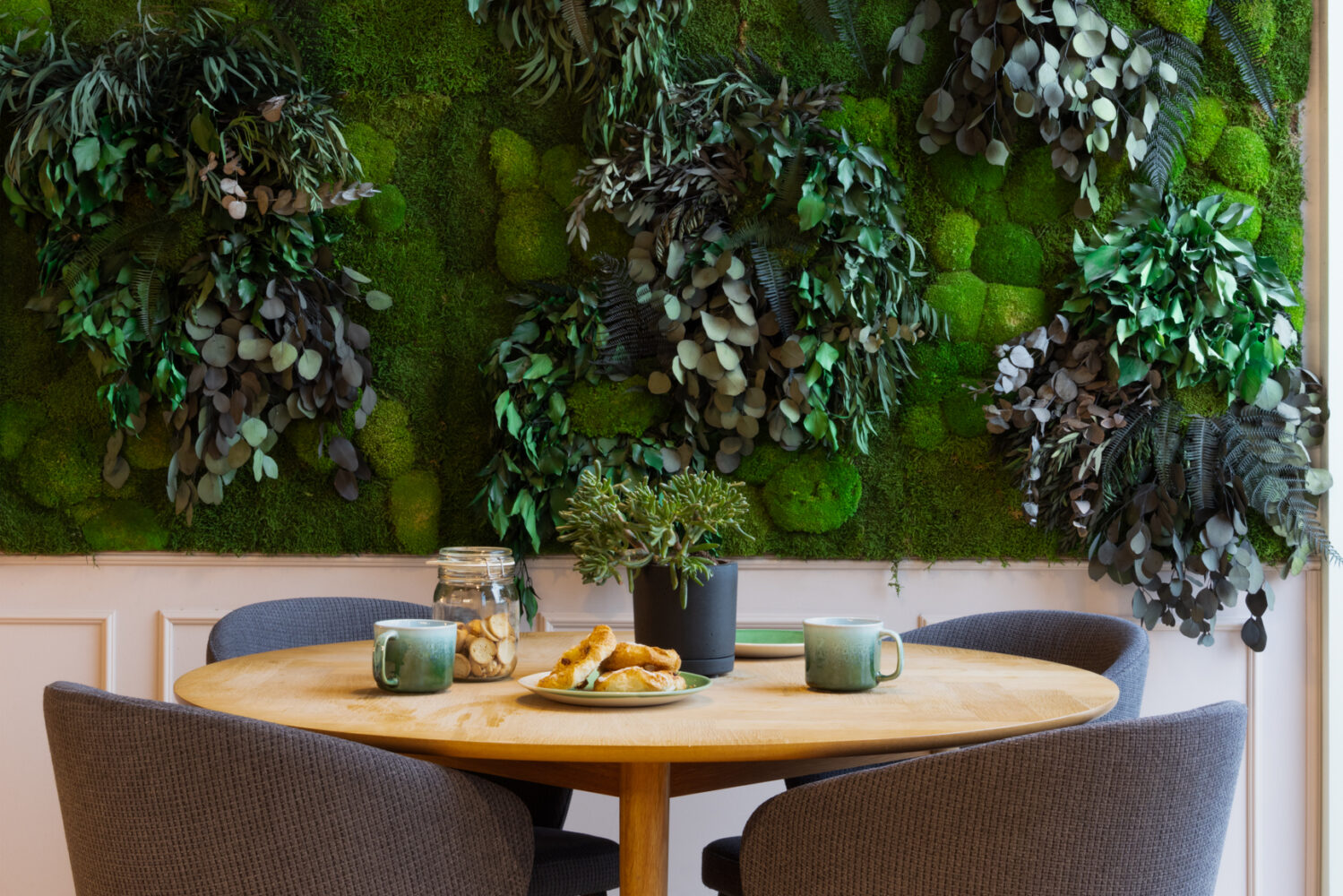 Table with 4 chairs in coffee area, in front of live green plant wall in BaseStack student accommodation and apartments to rent in Copenhagen