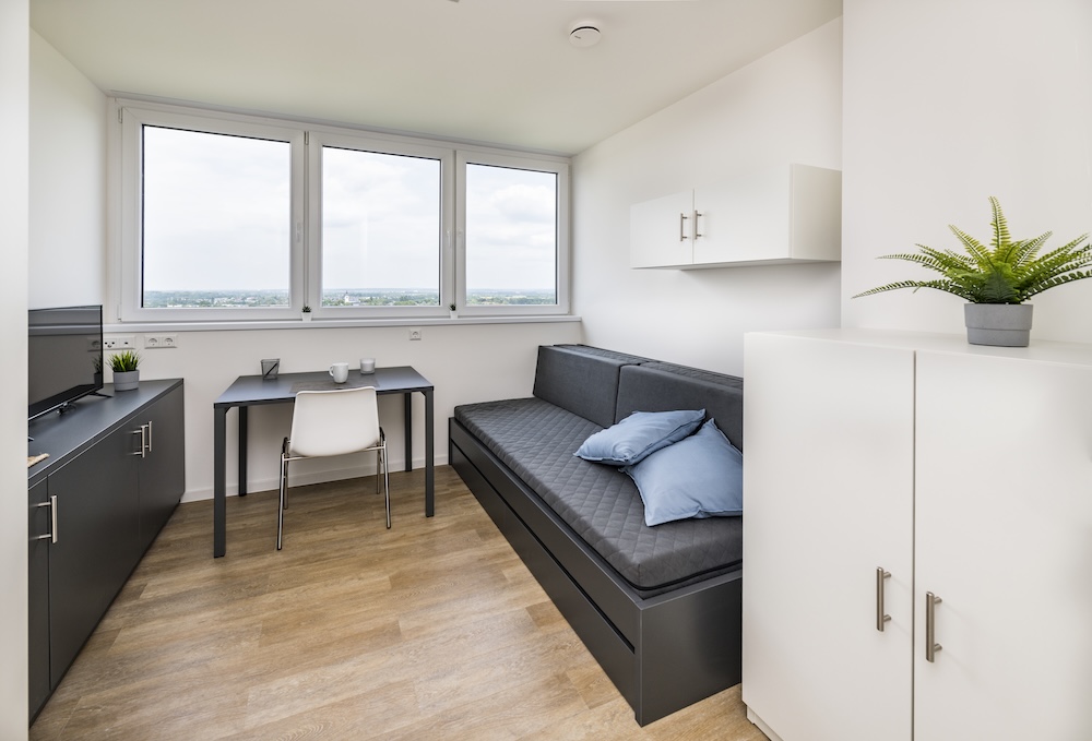 Studio with a sofa bed, dining table, kitchenette, storage cabinets and wide windows at MILESTONE Bonn.