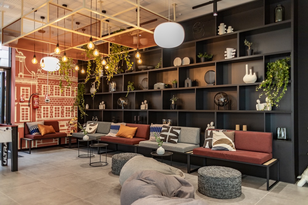 Social lounge with red bench seating, grey beanbags, black shelving and hanging plants.