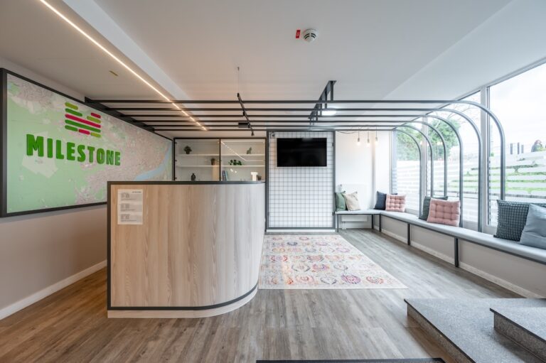 Reception lounge at student accommodation MILESTONE Bonn with a curved desk, long window bench, branded map wall and television.