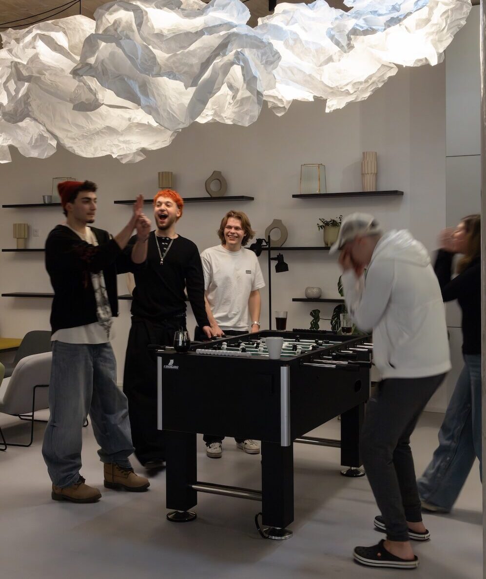 Students playing table football in the MILESTONE Erdberg games area, with lounge seating visible behind.