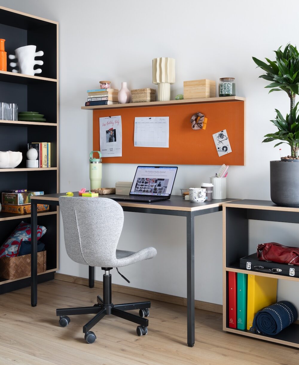 Giant Studio workspace at MILESTONE Erdberg student housing with a desk, orange pinboard, open shelving and leafy plants.