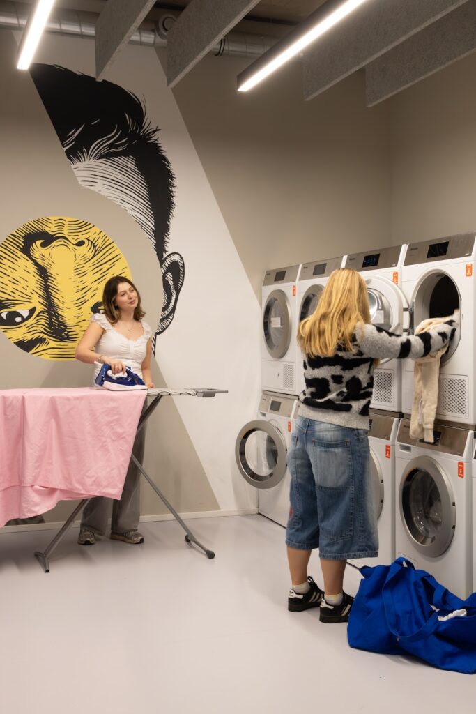 Residents using the laundry facilities in student housing in Vienna, with an ironing station and two banks of machines.