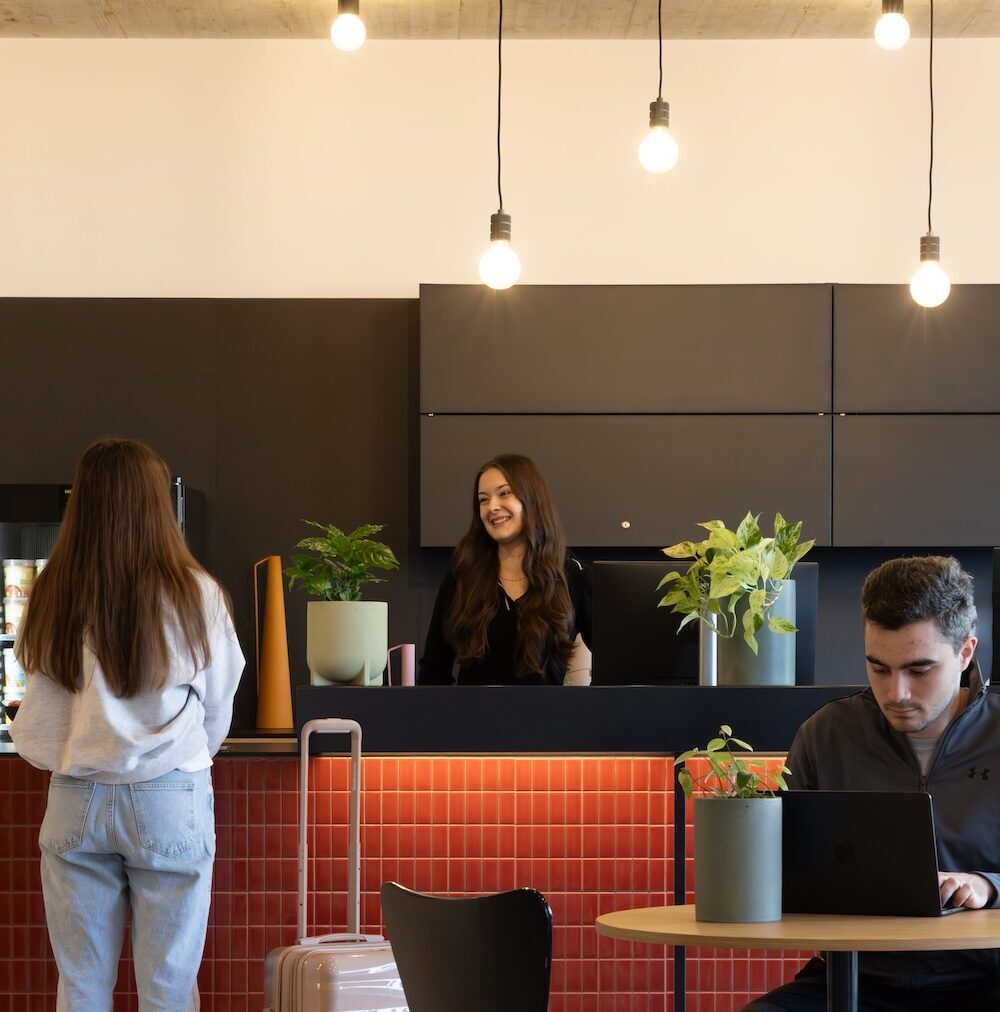Reception desk for student apartments in Vienna Erdberg with a red tiled counter, pendant lights and residents checking in.