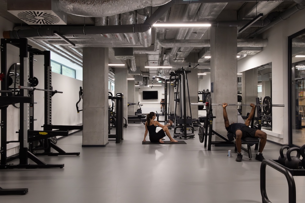 Gym in student housing in Krakow with cable machines, weights and open training space and students exercising.