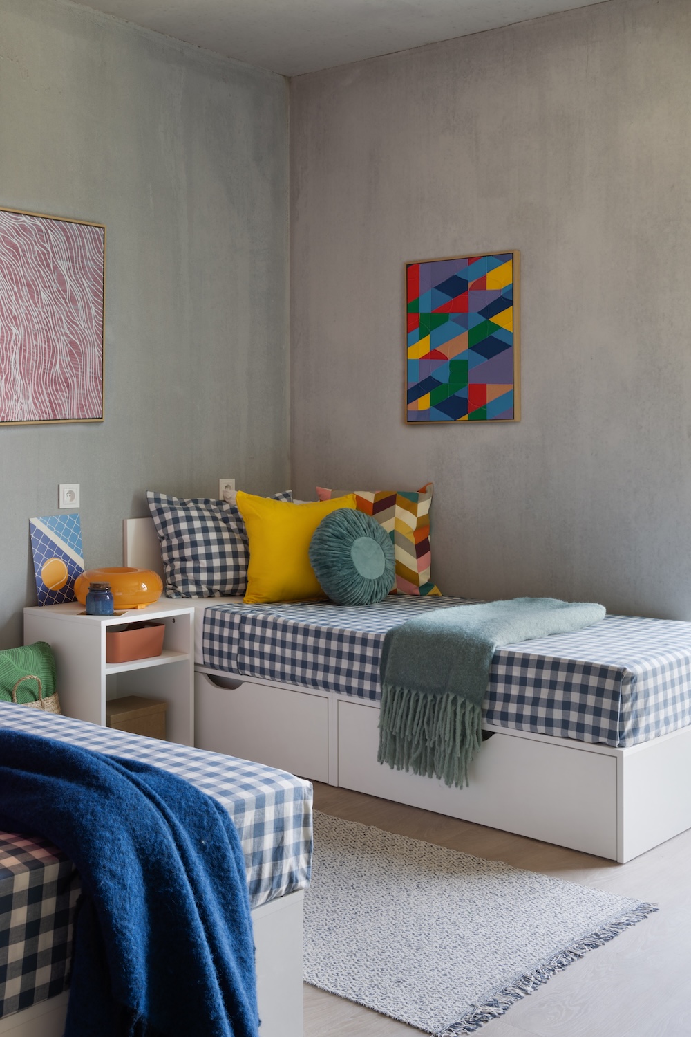 Twin daybeds for students at Milestone Warsaw with checked bedding, colourful cushions and concrete-effect walls.