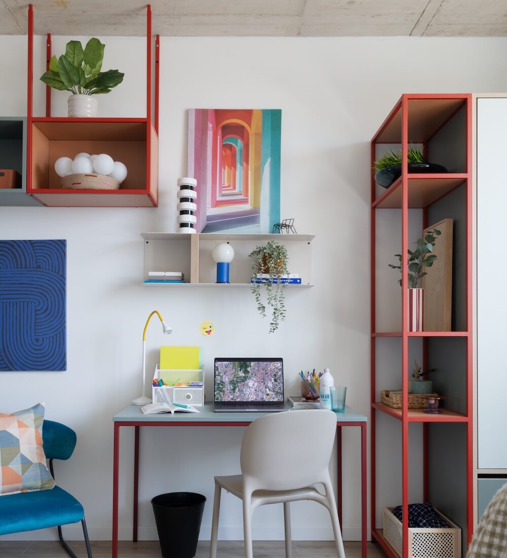 Desk, task lamp, colourful shelving and wall artwork at Tribera student accommodation in Milan.