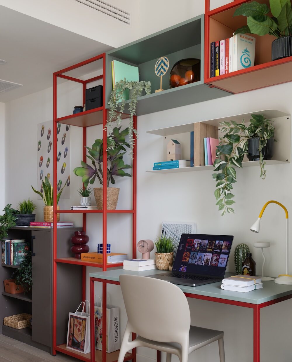 Desk with red shelving, plants and a laptop at Tribera student accommodation in Milan.